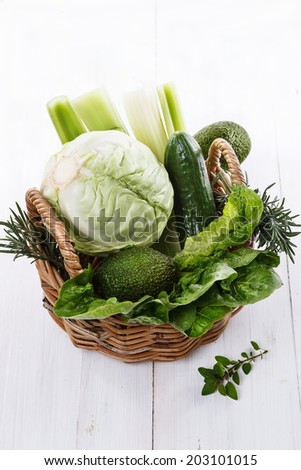 Fresh organic green vegetables in a woven basket on white wooden background