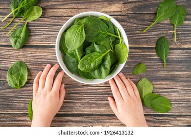 Fresh Organic Healthy Spinach In White Bowl Overhead Shot With Young Child White Caucasian Hands Holding White Bowl On Wood Texture Table Background