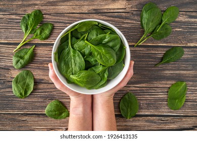 Fresh Organic Healthy Spinach In White Bowl Overhead Shot With White Female Hands Holding White Bowl On Wood Texture Table Background