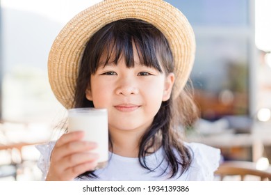 Fresh organic lactose free milk on glass.Asian cute little girl drinking milk.Calcium vitamin from milk.Grocery food.Good taste.Kid drink goat milk.School kid girl wearing straw hat.Delicious tasty.