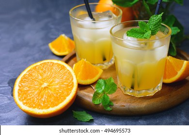 Fresh Organic Orange Juice In Glass With Ice And Mint Leaf Decorated By Cut Orange Fruits On Wooden Tray.