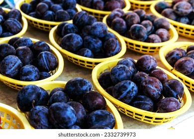 Fresh organic plums in yellow plastic baskets on display at local farmers market - Shutterstock ID 2332739973
