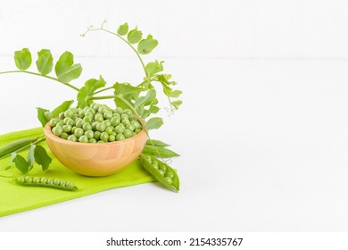 Fresh Organic Raw Green Peas In A Wooden Bowl With Peas Plants Leaves On A Napkin On White Background. Healthy Eating, Vegan And Vegetarian Legume Food, Raw Food And Detox Super Food, Bean Protein