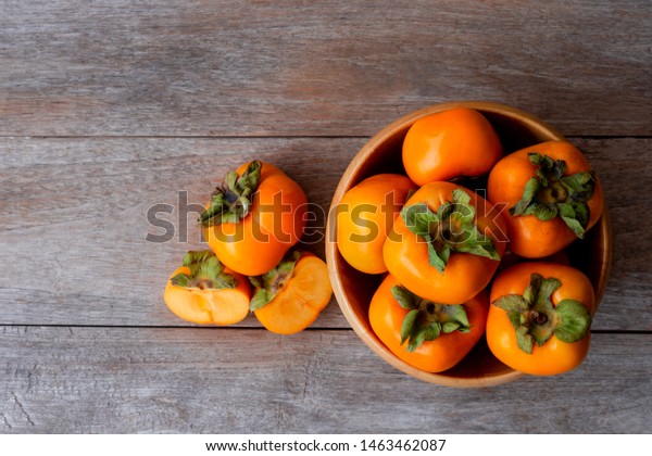 Fresh organic ripe Persimmons fruits in\
wooden bowl with slice isolated on old wooden table background. Top\
view. Flat lay. Copy space for text and\
content.