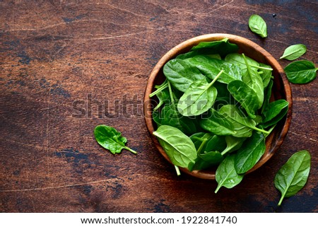 Fresh organic spinach leaves in a wooden bowl over dark rustic background. Top view with copy space.