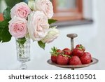 Fresh and organic strawberries from the garden in a silverware on the marble table with roses . Vase for flowers . Romantic terrace. Love  