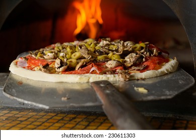 Fresh original Italian pizza on a shovel is putting in a traditional wood-fired stone oven.