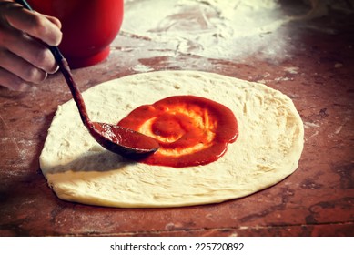 Fresh original Italian raw pizza, dough preparation in traditional style. Applying a tomato sauce.