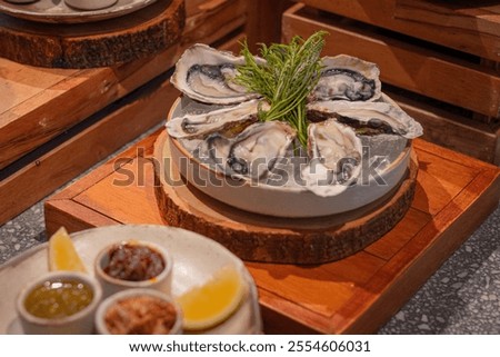 Fresh oyster arranged on ice and garnished with green herbs on round dish with crispy fried onion, seafood sauce and chili paste