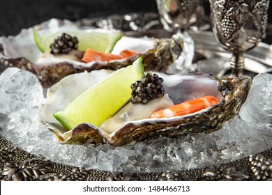 Fresh oysters with black sturgeon caviar and shrimp in ice, with lime in a luxurious serving in a silver plate with vodka in silver shot glasses.