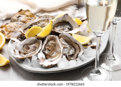 Fresh oysters with lemon and glasses of champagne on grey table, closeup