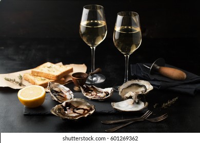Fresh oysters with lemon and glasses of wine on a dark background