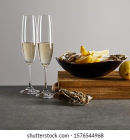 fresh oysters and lemons in bowl near champagne glasses with sparkling wine isolated on grey 