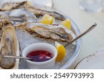 Fresh oysters on the halves of the shell are served in a plate with ice, lemons and sauce.