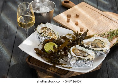 Fresh oysters on ice with algae and lemon with white wine on black wooden background.
