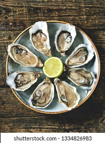 Fresh oysters with slices of lemon on ice on old wooden background. Top view. 