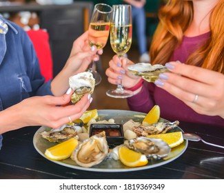 Fresh oysters as well as fine dining, two young attractive woman eating oysters in restaurant and drinking champagne. Eating out concept, dinner in restaurant.