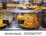 Fresh Paella and different Spanish food, goods on a street food market. Huge pots with various types of paella on a counter at the central market