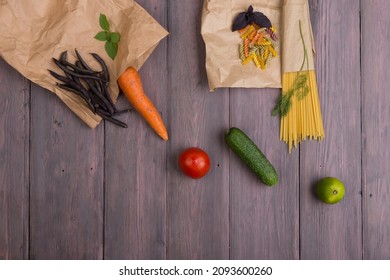 Fresh pasta ingredients in eco paper bags - spaghetti pasta, carrot, basil, tomato and other vegetables on wooden table