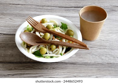 Fresh pasta salad in disposable compostable chinet plate, eco friendly disposable biodegradable brown cutlery with disposable kraft on wooden table - eco environmental friendliness concept  - Powered by Shutterstock