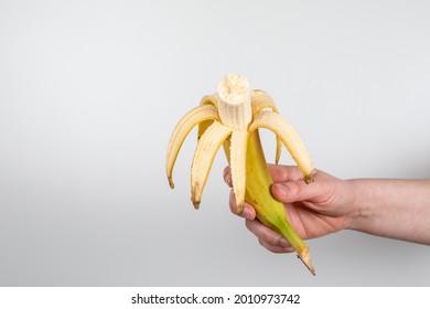 Fresh peeled bitten banana in a woman's hand on a white background.