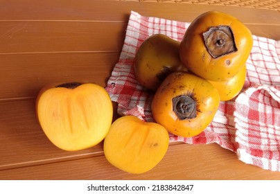 Fresh Persimmons That Have Been Cut And Whole Persimmons On A Red And White Cloth On A Wooden Textured Plastic Table, Selected Focus