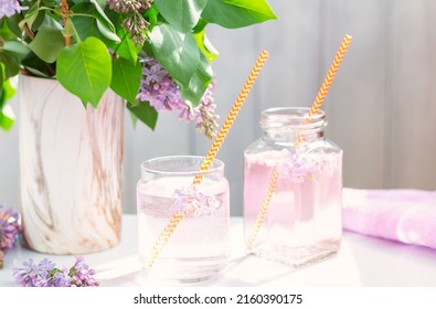 Fresh pink non alcoholic cocktail in glass with lilac flowers and orange straws for cocktails on white background, copy space for text. lilac refreshing drink, selective focus, high key, daylight - Shutterstock ID 2160390175