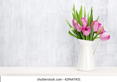 Fresh pink tulip flowers bouquet on shelf in front of wooden wall. View with copy space