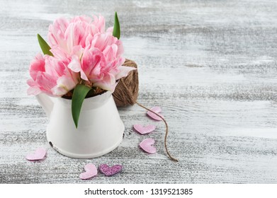 Fresh pink tulip flowers in jug, hearts and twine on rustik wooden background