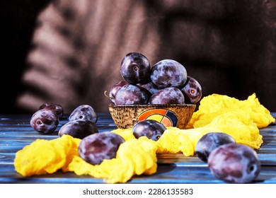 Fresh plums in clay bowl and yellow gauze on old rustic blue wooden table at sunlight - Powered by Shutterstock