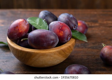Fresh plums with leaves in a wooden bowl on a brown table. Gathering the summer harvest.