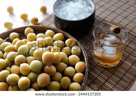 Fresh plums, rock sugar and plum wine in a clear glass on a wooden table. Ingredients for making plum wine or Umeshu and plum syrup.