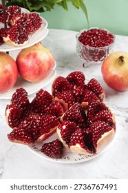 Fresh pomegranates with seeded arils displayed on white marble surface with soft green background, rich in vitamins and healthy nutrients.