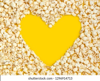 Fresh popcorn heart shaped close-up on a bright yellow background, top view.
