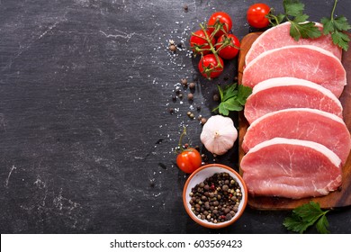 fresh pork with ingredients for cooking on dark background