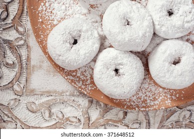 Fresh powdered sugar donuts in rustic setting with hand-thrown pottery plate and distressed wood serving tray.  Closeup from above with soft natural lighting for a vintage feel.