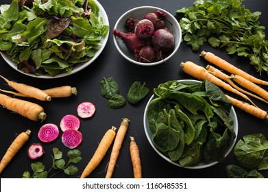 Fresh produce from the local farm including mixed greens, spinach, carrots, and beets on black background.