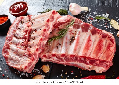 fresh rack of raw pork spare ribs seasoned with spices on black slate tray with paprika, garlic cloves, bay leaves at background, vertical view from above, close-up - Powered by Shutterstock