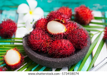 Fresh rambutans in a grey stone bowl on wooden colorful background.
