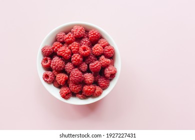 Fresh raspberries in white bowl on pastel pink background. Flat lay, top view, copy space