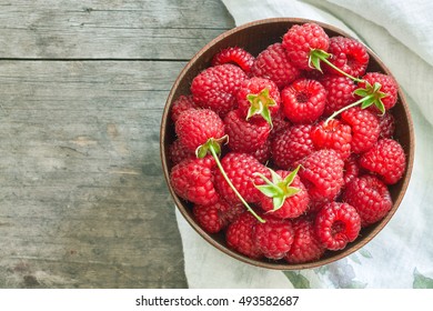 Fresh raspberries in wooden bowl on grey rustic wooden background. Top view with copy space