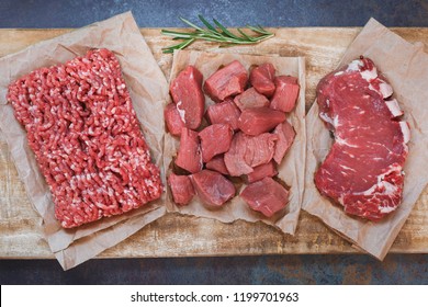 Fresh raw angus beef meat, whole, ground and chopped on parchment paper , wooden cutting board,  stone background, top view