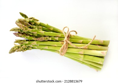 Fresh raw asparagus bunch tied with string in flat lay format on white background with copy space