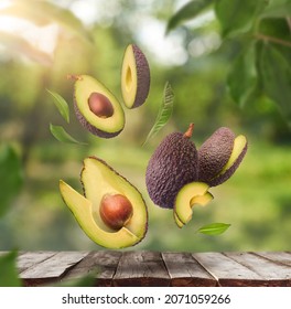 Fresh Raw Avocados Falling In The Air On Wooden Table Over Defocused Bokeh Background. Food Levitation Concept. Zero Gravity Fruit Conception. High Resolution Image