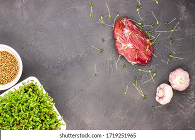 fresh raw beef, dotted with green sprouts of flax microgrid and vegetables with spices on a black marble background, top view. green flax sprouts with red meat