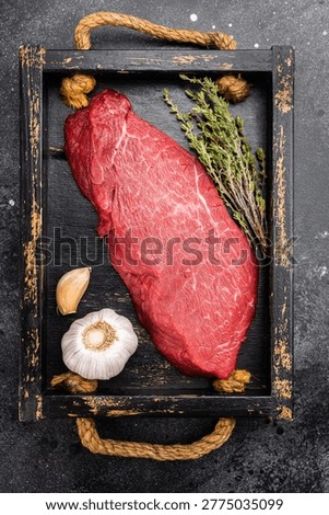 Fresh raw beef inside round topside with thyme herb and garlic on wooden tray. Lean butcher cut meat on dark background, top view