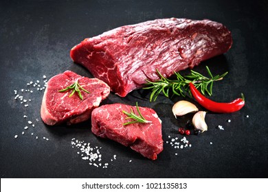 Fresh and raw beef meat. Whole piece of tenderloin with steaks and spices ready to cook on dark background 