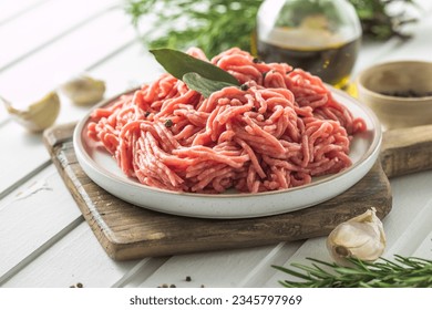 Fresh Raw Beef Minced Meat with herbs and rosemary on wooden board on a light background, banner, menu, recipe place for text, top view,