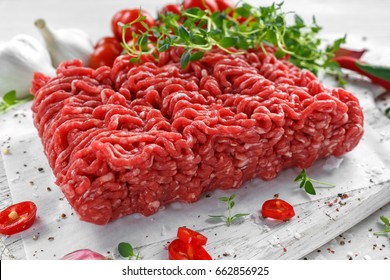 Fresh Raw Beef Minced Meat with salt, pepper, chilli and fresh thyme on white board.