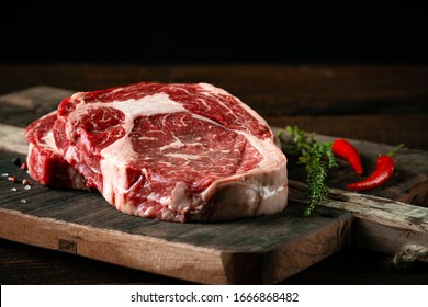 Fresh raw beef rib eye steak with red pepper and herbs on a wooden background
